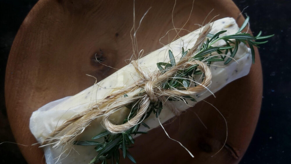 Domaći aromatizirani maslac s paprom i Dijon senfom, zamotan u papir i ukrašen grančicom ružmarina
